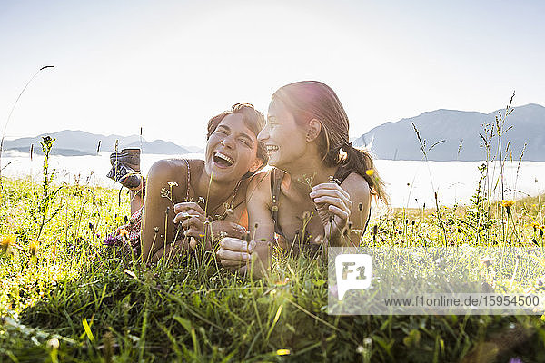 Two happy female friends lying on a meadow in the mountains  Achenkirch  Austria