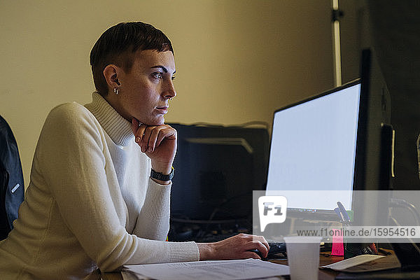 Rothaarige junge Frau benutzt Computer am Schreibtisch