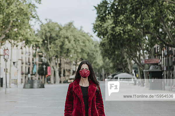 Porträt einer Frau mit roter Gesichtsmaske und Jacke  die auf einer leeren Straße in der Stadt steht  Barcelona  Spanien