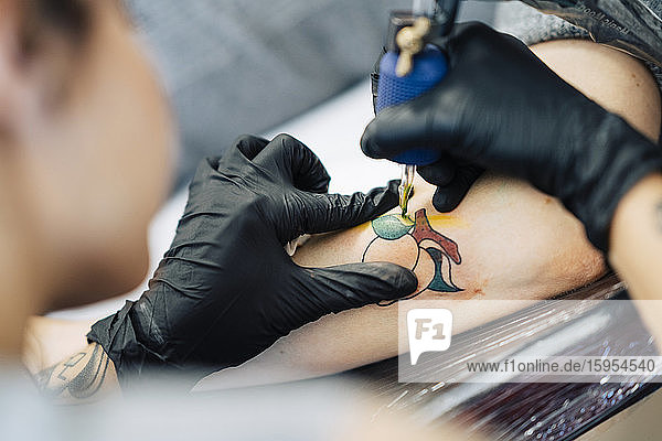 Female tattooist tattooing on a woman's arm