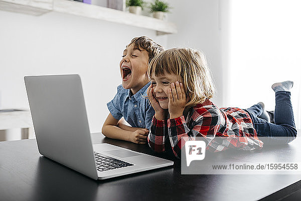 Glückliches Mädchen und Junge liegen auf dem Schreibtisch und schauen auf den Laptop