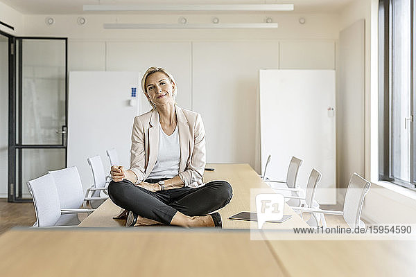 Blond businesswoman sitting on table in conference room