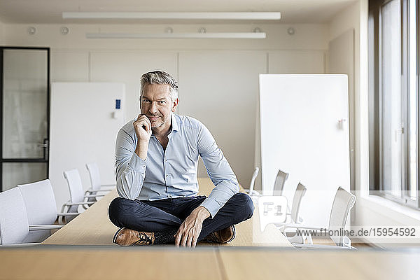 Portrait of confident mature businessman sitting on table in conference room