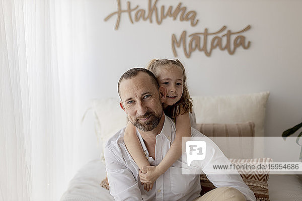 Porträt eines kleinen Mädchens  das seinen glücklichen Vater zu Hause umarmt