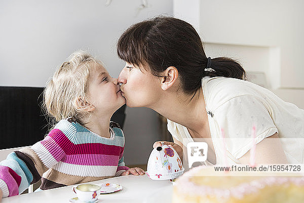 Mutter und Tochter spielen mit dem Puppengeschirr  küssen sich gegenseitig
