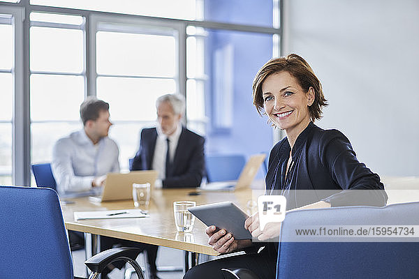 Porträt einer lächelnden Geschäftsfrau mit Tablette während einer Besprechung im Büro