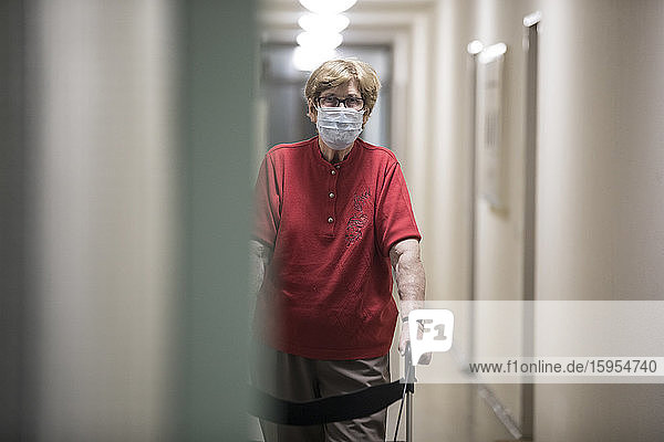 Ältere Frau mit Maske und Gehhilfe auf Rädern im Flur des Altenheims