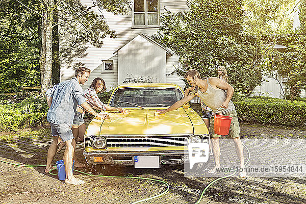 Eine Gruppe von Freunden wäscht im Sommer einen gelben Oldtimer