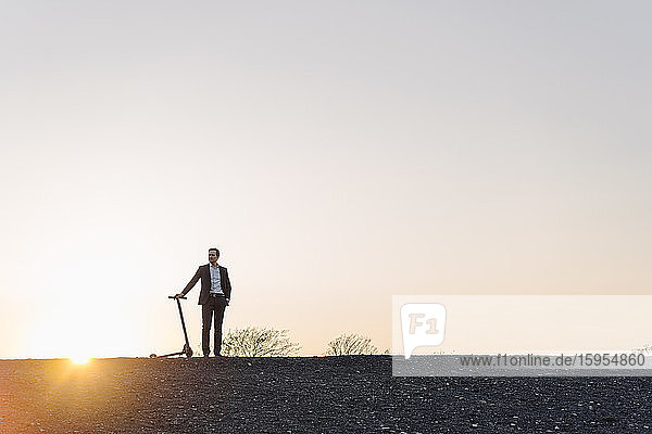Mature businessman with a kick scooter on a disused mine tip at sunset