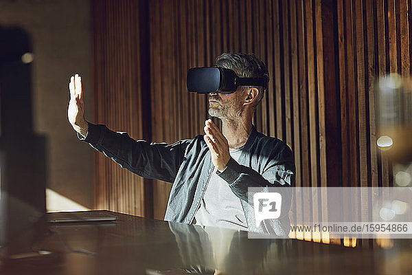 Lässiger Geschäftsmann  der in seinem nachhaltigen Büro sitzt und durch eine VR-Brille schaut