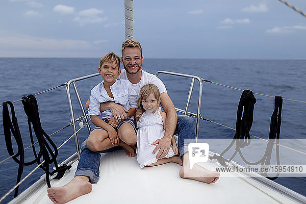 Vater mit seinen Kindern während der Segelfahrt auf dem Bootsdeck sitzend