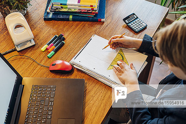 Junge sitzt am Schreibtisch mit Laptop und Notizbuch
