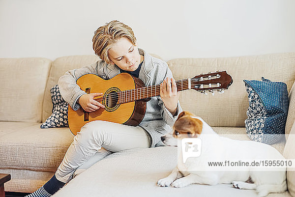 Boy with dog playing guitar on couch at home