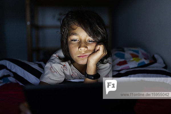 Portrait eines gelangweilten Jungen,  der zu Hause auf dem Bett liegt und ein digitales Tablett benutzt