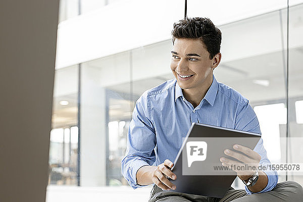 Portrait of smiling young businessman with tablet at the window in office