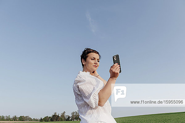 Portrait of smiling woman taking selfie with smartphone on a field