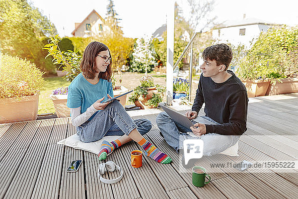 Teenager-Paar sitzt auf der Terrasse und lernt zusammen mit Laptop und digitalem Tablett