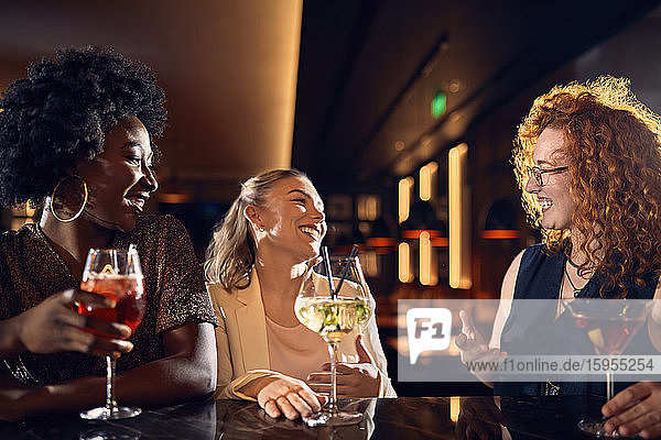 Happy friends socializing in a bar with cocktails
