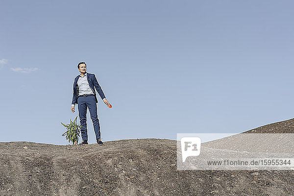 Mature businessman with a plant standing on a disused mine tip