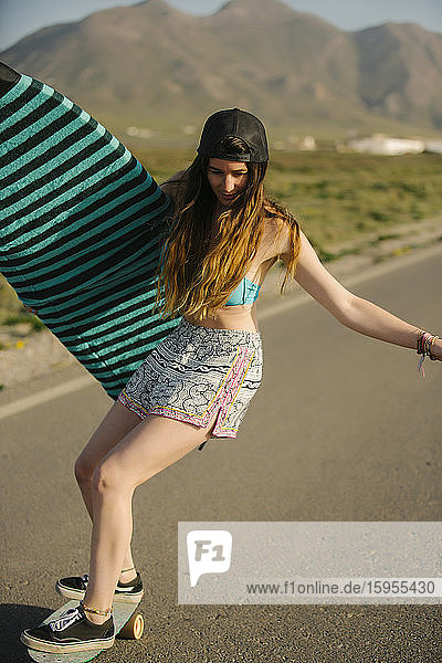 Young woman with surfboard skateboarding on asphalt road  Almeria  Spain