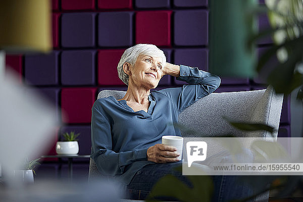 Porträt einer lächelnden älteren Geschäftsfrau  die auf einem Sessel sitzt und in die Ferne schaut