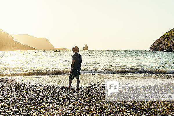 Back view of man standing on the beach looking to sea at sunset  Cala Benirras  Ibiza  Spain