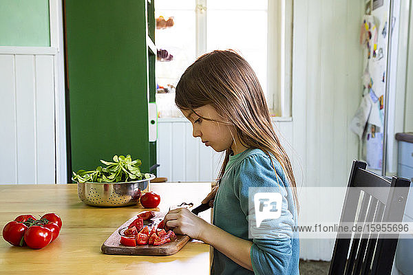 Mädchen schneidet Tomaten auf dem Schneidebrett in der Küche
