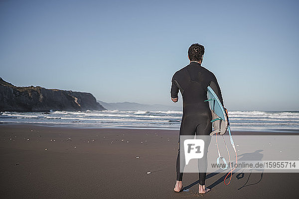 Rückansicht eines behinderten Surfers mit Surfbrett am Strand
