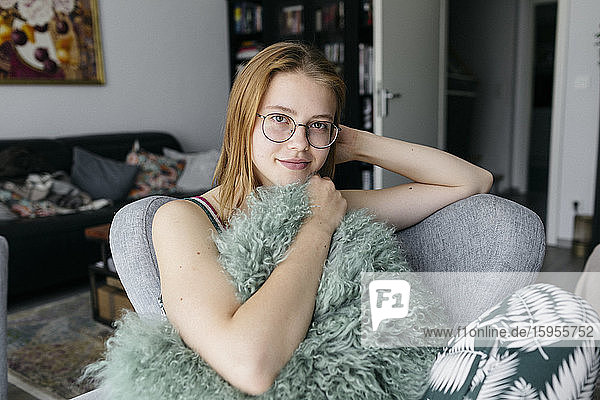 Porträt einer lächelnden jungen Frau  die auf einem Sessel im Wohnzimmer sitzt
