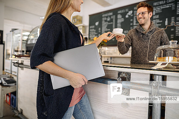 Young woman with laptop in a cafe ordering a cup of coffee
