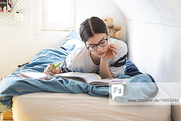 Girl lying on bed doing homework