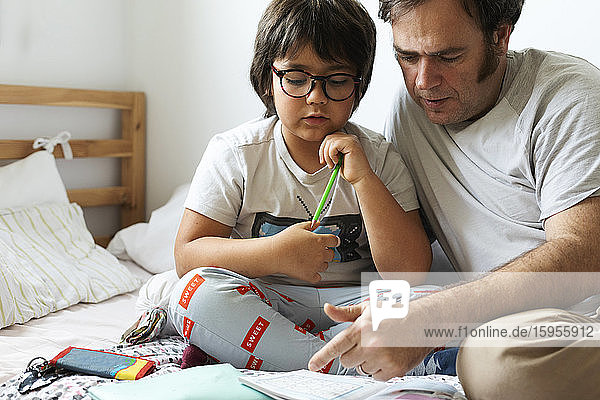 Vater hilft dem Sohn bei den Hausaufgaben  während er zu Hause im Bett sitzt