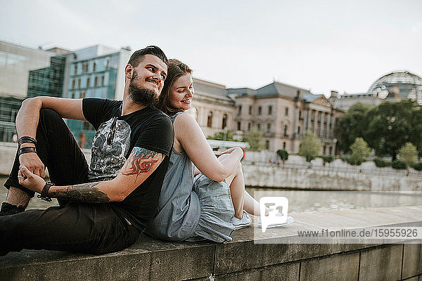 Young couple sitting on a wall at the riverbank  Berlin  Germany
