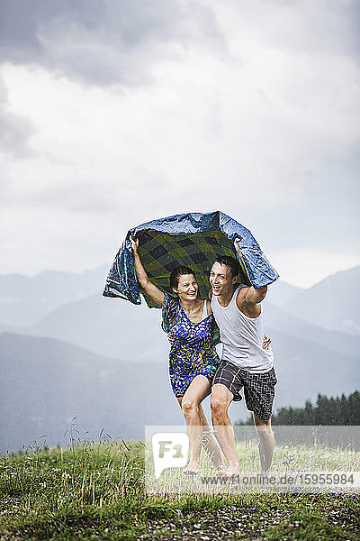 Happy couple running on a meadow in the mountains in rain  Achenkirch  Austria