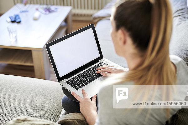 Hochwinkelansicht einer Frau  die einen Laptop benutzt  während sie zu Hause auf dem Sofa sitzt