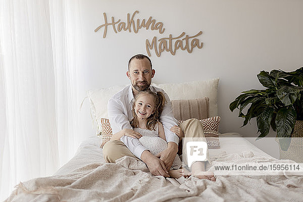 Porträt eines glücklichen Vaters und seiner kleinen Tochter  die zusammen auf dem Bett sitzen