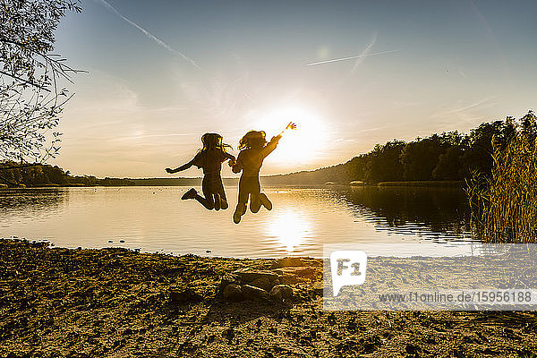 Freunde springen in die Luft und genießen am Seeufer bei Sonnenuntergang