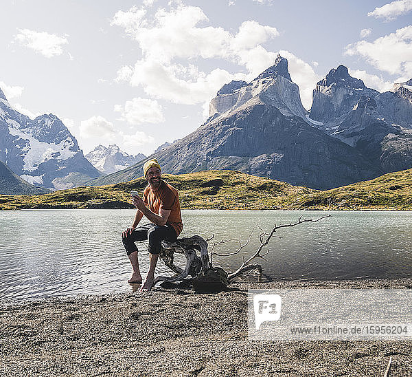 Mann hält Mobiltelefon in der Berglandschaft am Seeufer im Nationalpark Torres del Paine  Patagonien  Chile