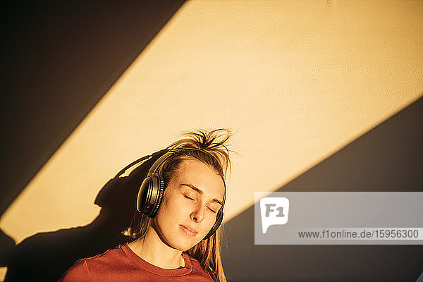 Porträt einer jungen Frau mit Kopfhörern bei Sonnenschein zu Hause