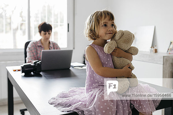 Mother working at home  daughter sitting with teddy bear on table