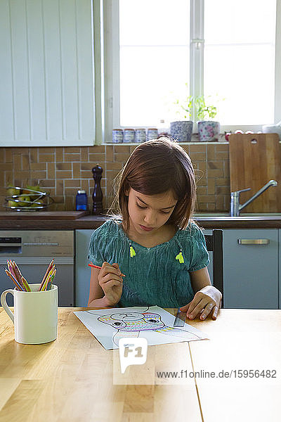 Kleines Mädchen sitzt am Küchentisch und zeichnet einen Osterhasen