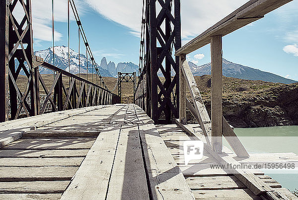 Iron and wood bridge on the water and Torres del Paine mountains at the background  Parque Nacional Torres del Paine  Chile