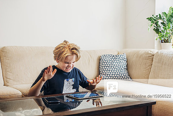 Frustrated boy with smartphone and tablet in living room