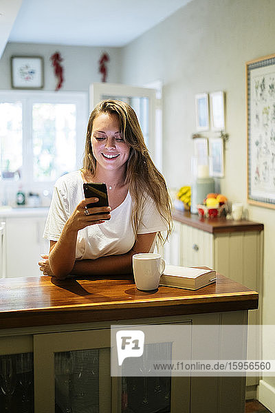 Junge Frau benutzt Smartphone in der Küche
