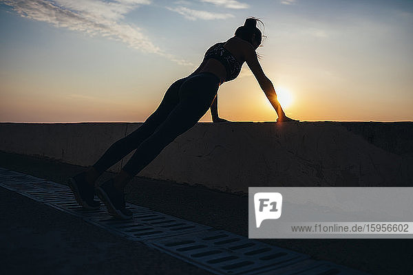 Silhouette woman doing push-ups at promenade during sunrise