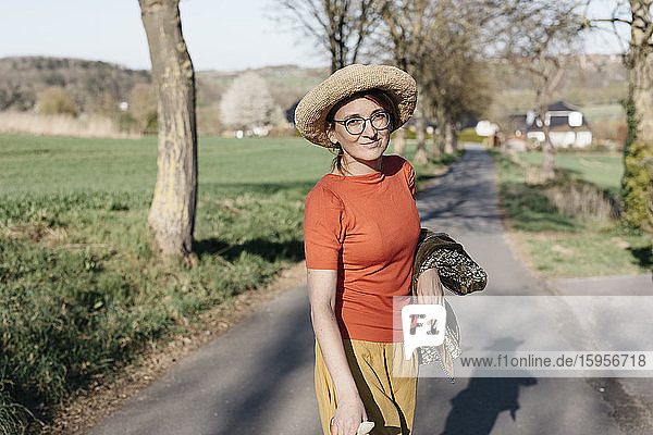 Porträt einer lächelnden reifen Frau mit Brille und Strohhut auf einer Landstraße stehend