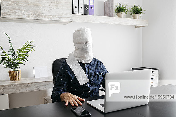 Man working at home with his head covered in toilet paper
