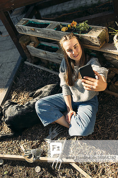 Happy young woman with dog in garden taking a selfie