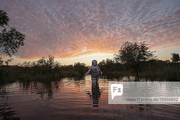 Spacewoman walking in water at sunset