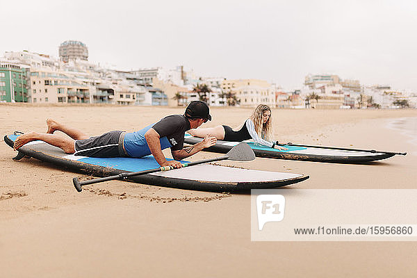 Instructor teaching young woman while lying on paddleboard at beach